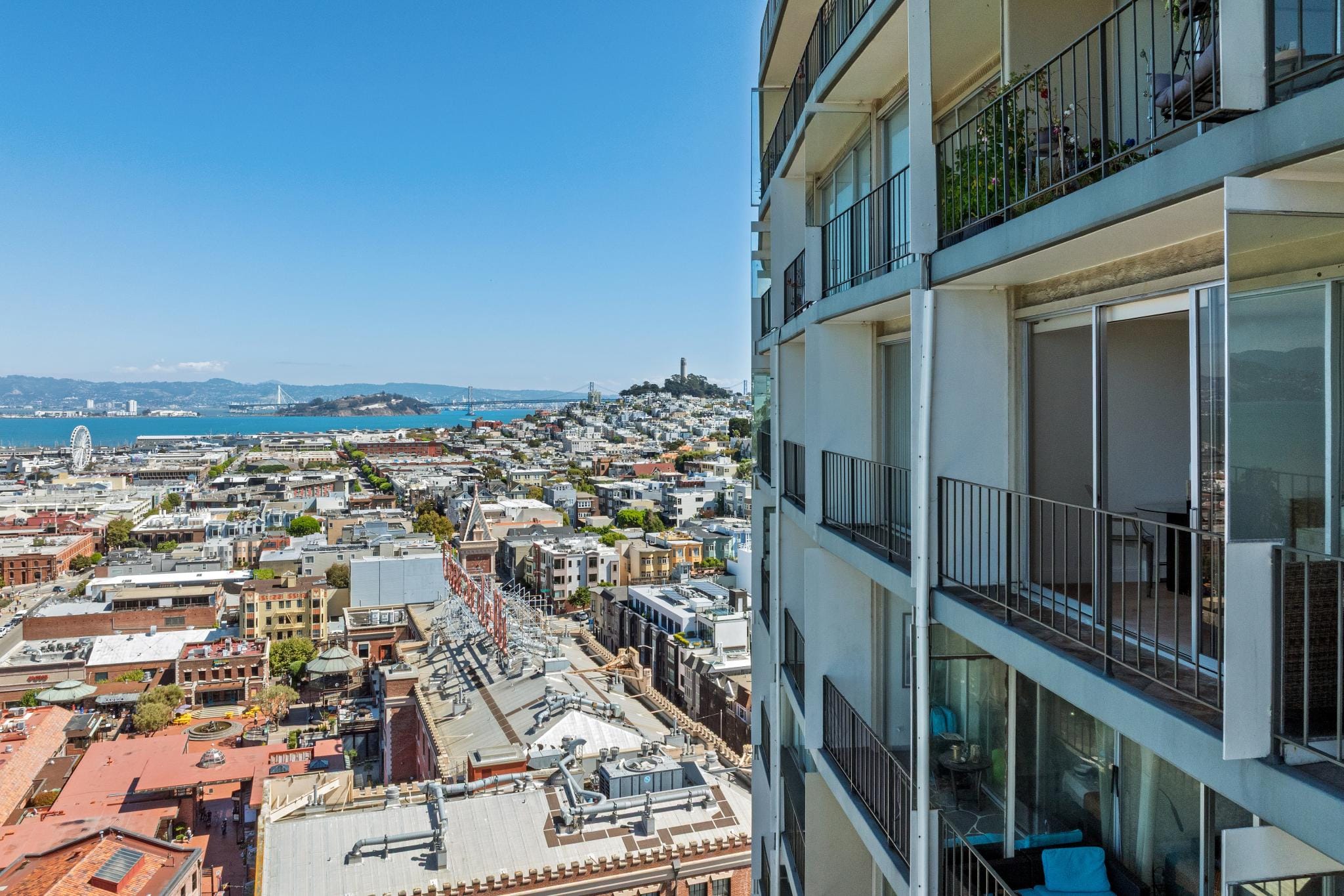 Close-up aerial photograph showing the balconies of 1000 North Point Street in San Francisco alongside a view of the surrounding North Beach neighborhood, Coit Tower, and the San Francisco Bay.