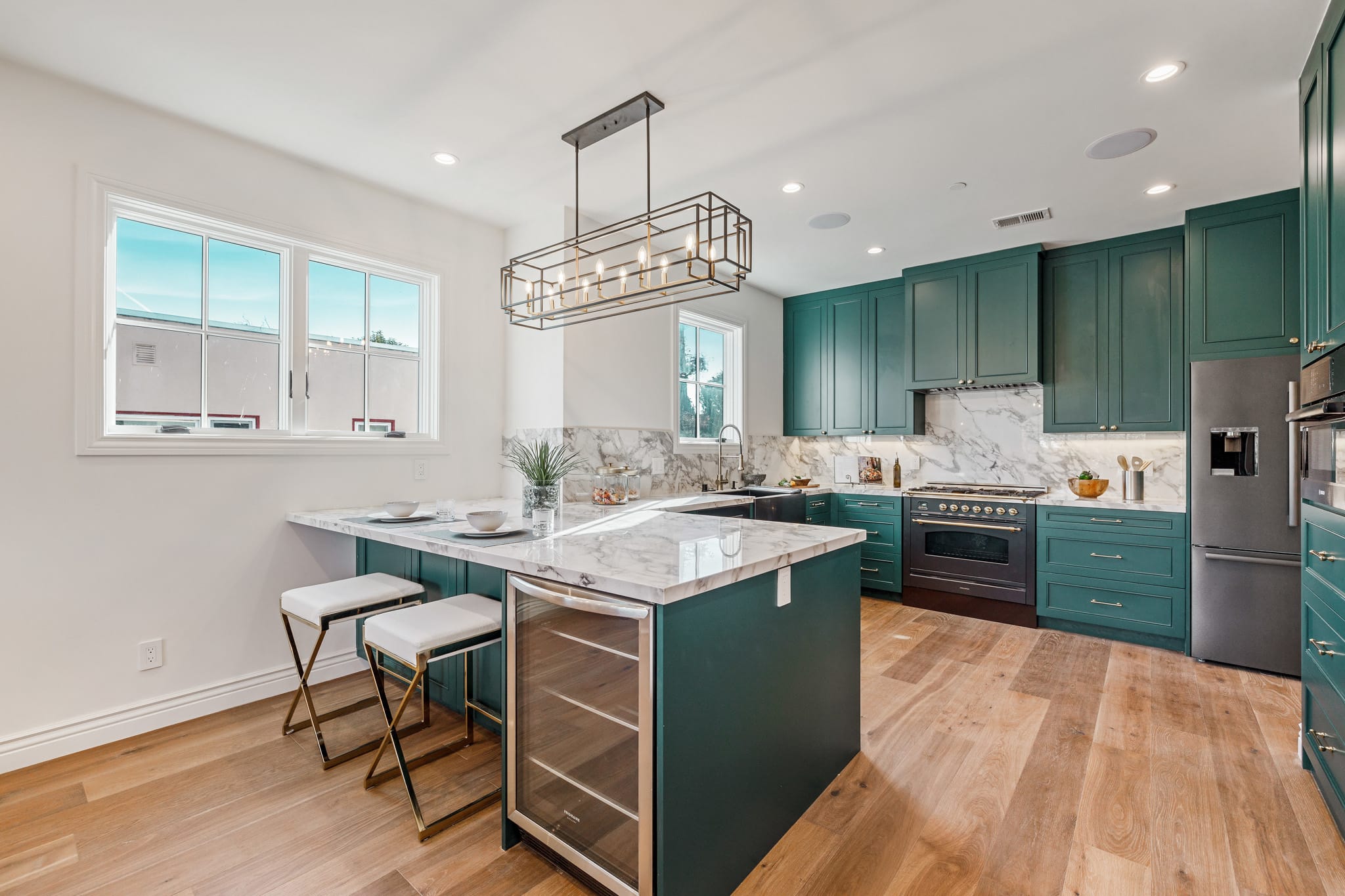 Full overview of teal sapphire kitchen with a wine cooler, bar seating, brass geometric pendant light, and black and stainless appliances at 115 Humboldt Road, Burlingame