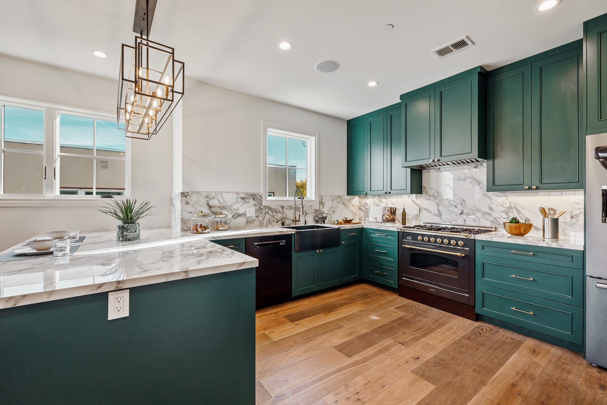 Teal sapphire kitchen island with marble countertop, brass geometric pendant light, and farmhouse sink in background
