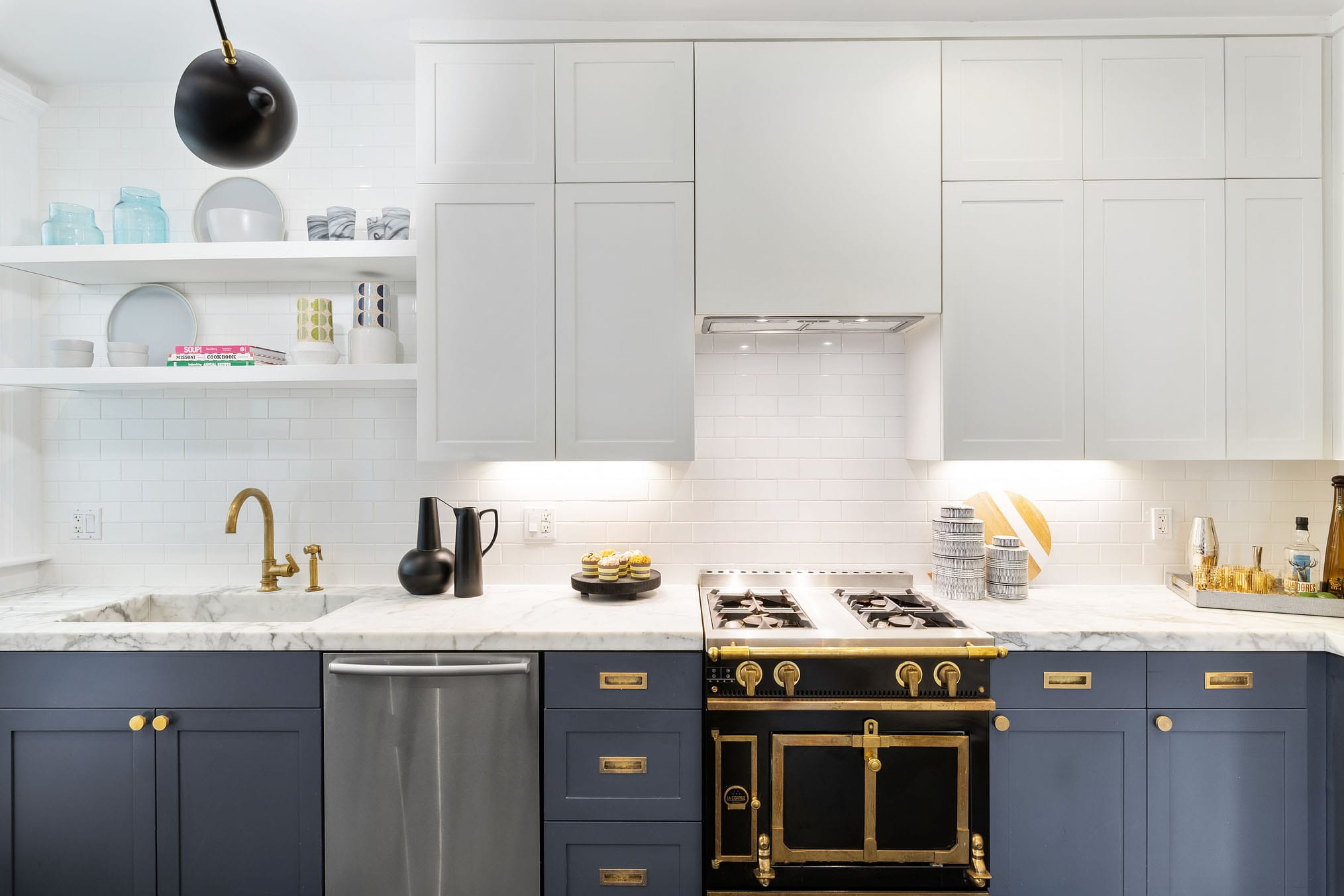 La Cornue Château black range with aged brass hardware and dusty, blue-gray lower cabinets with white uppercabinets.