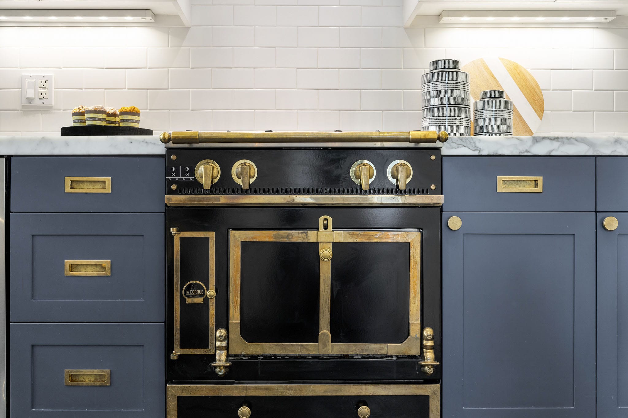 La Cornue Château black range with aged brass hardware and dusty, blue-gray cabinets.