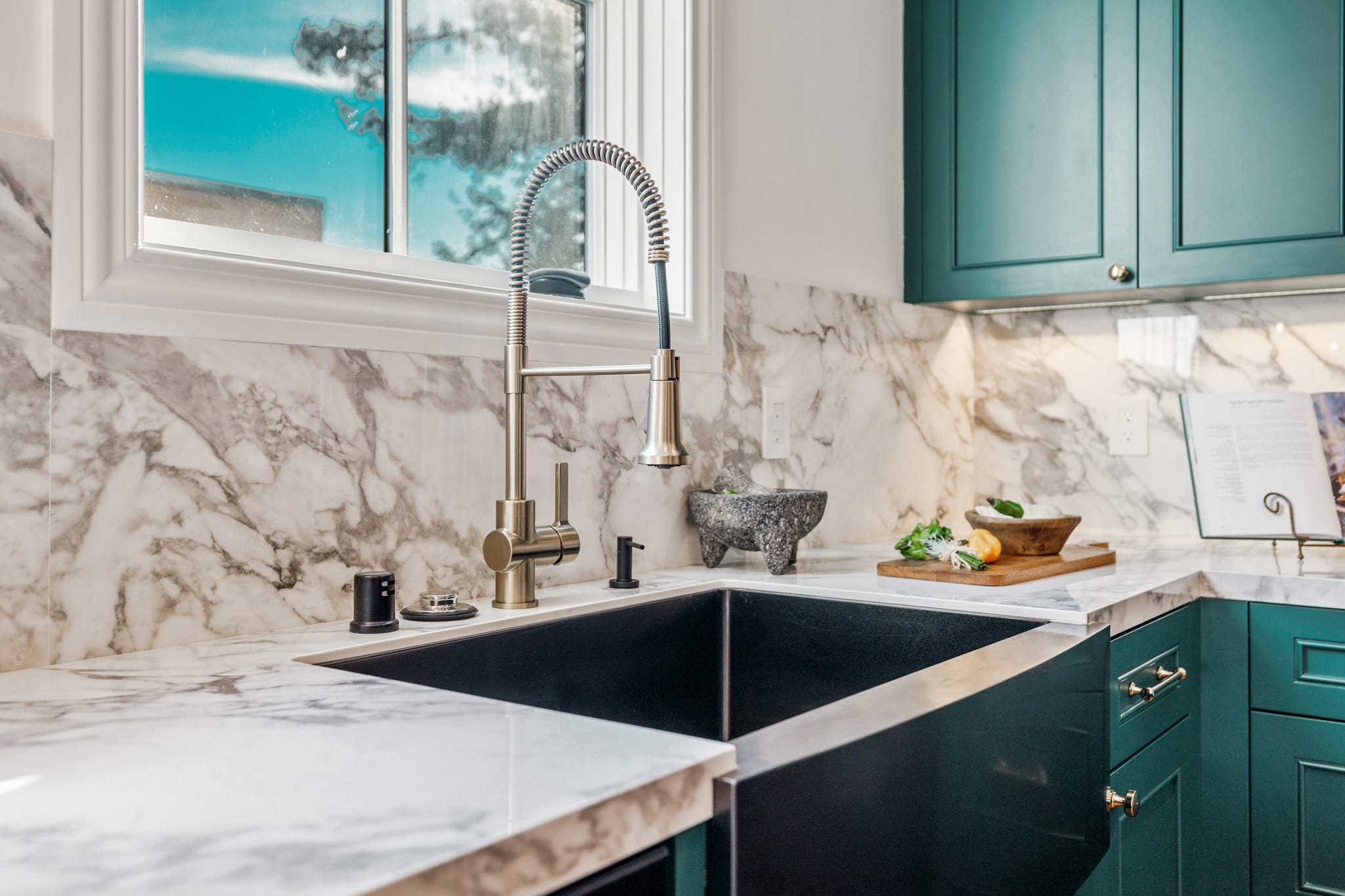 Stainless steel undermount farmhouse sink with brass spring faucet and marble countertop in teal kitchen