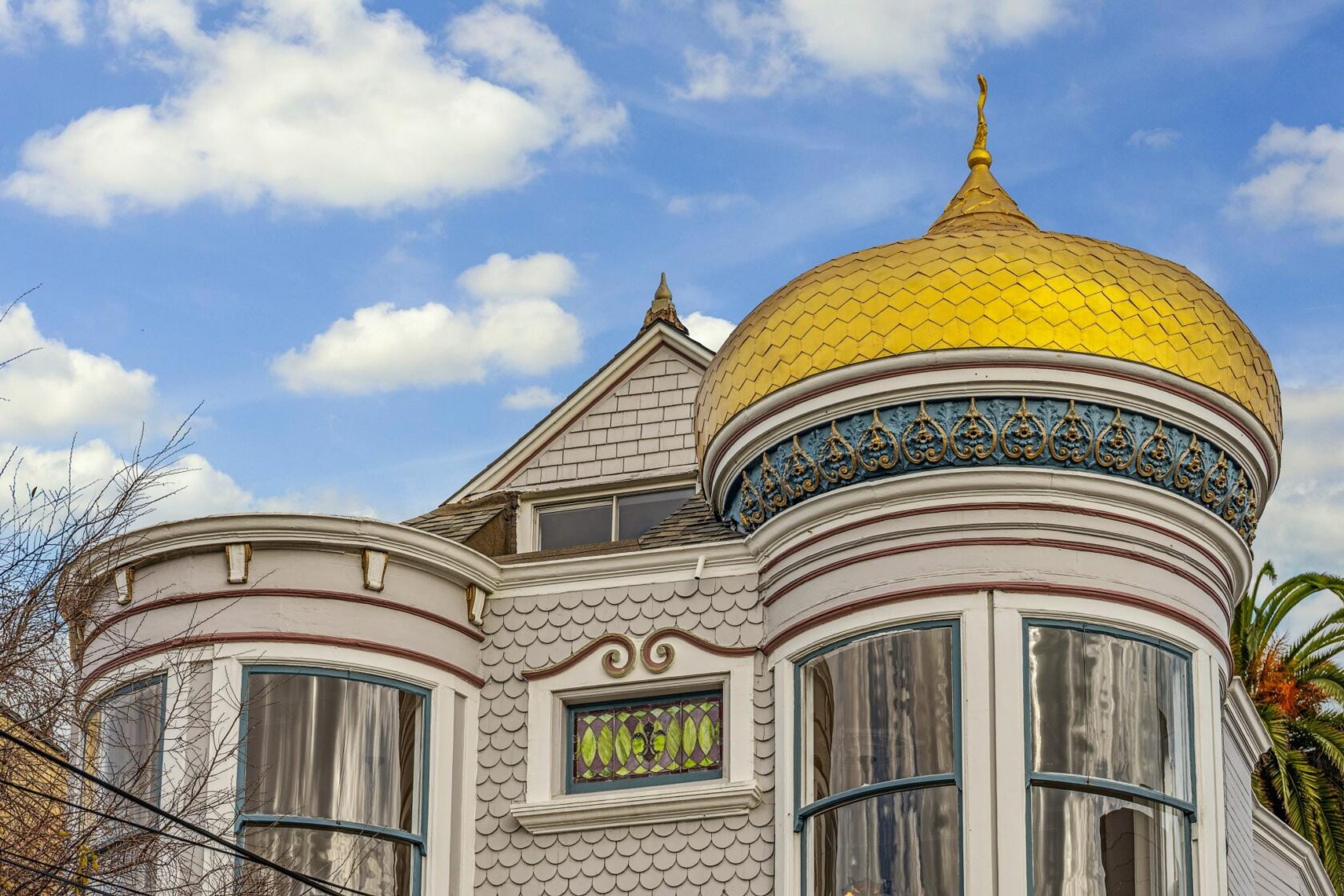 Upward view of the McCormick House's rounded turret with fish-scale shingle siding, curved bay windows, a colorful stained glass window, and the gold dome rising above the roofline.