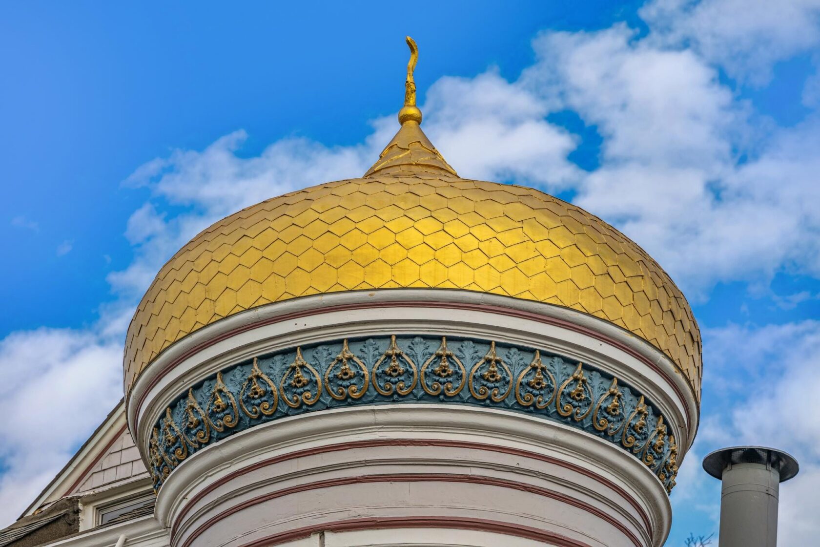 Close-up of the McCormick House's gilded onion dome with hexagonal gold tiles, intricate blue and gold filigree banding, and a curved finial against a bright blue sky.