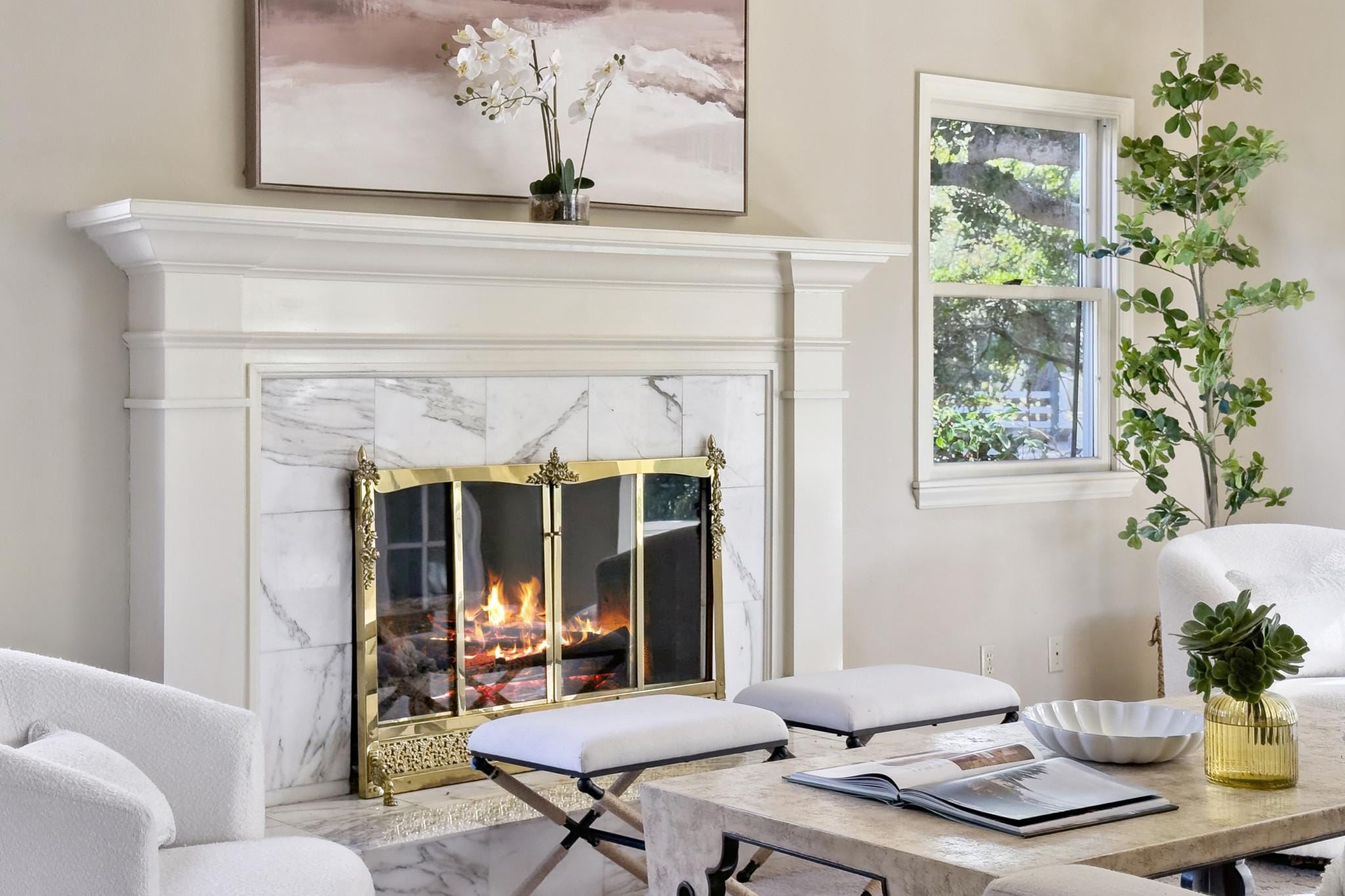 Living room fireplace with marble surround, white painted mantle, brass screen, and active fire in a Carmel-by-the-Sea home.