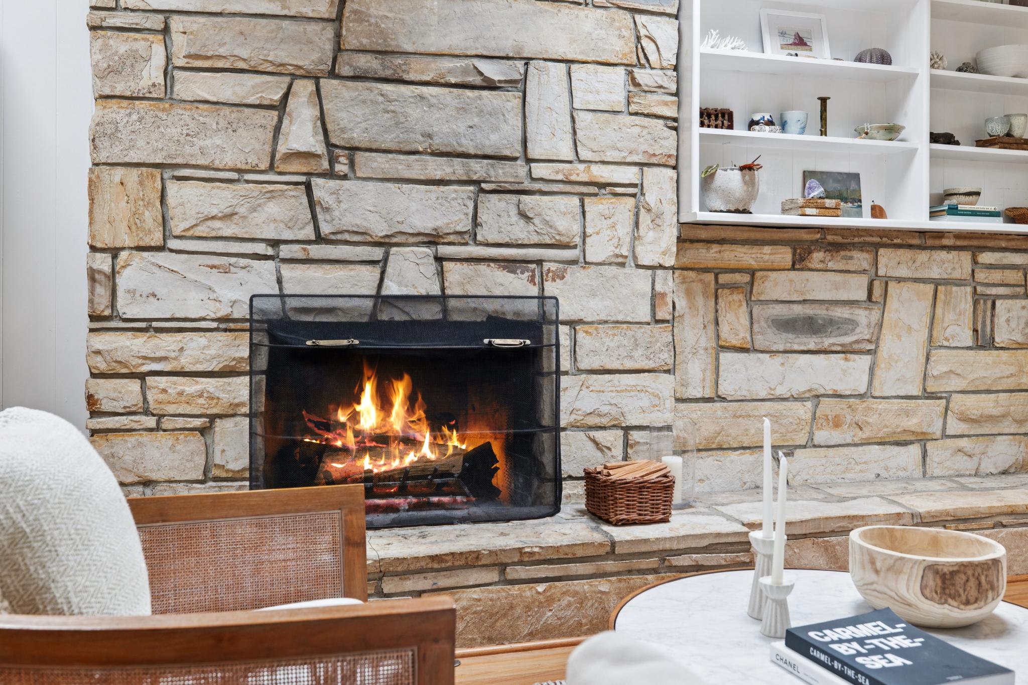 A wood-burning fireplace with active fire and built-in shelving in a Carmel-by-the-Sea cottage living room.