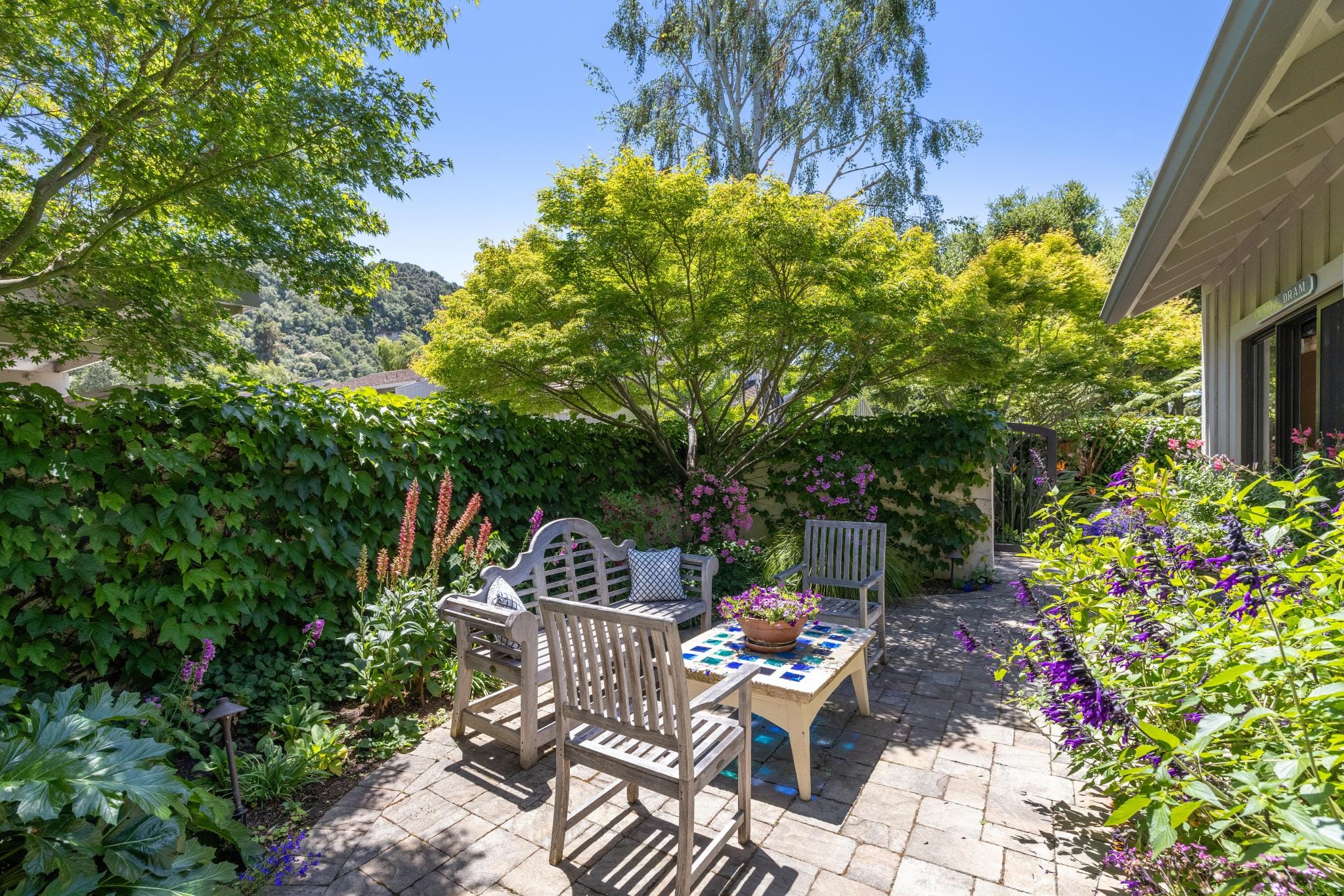 Private patio with wood benches, mosaic tile table, and lush flowering garden at a Carmel Valley Ranch home.