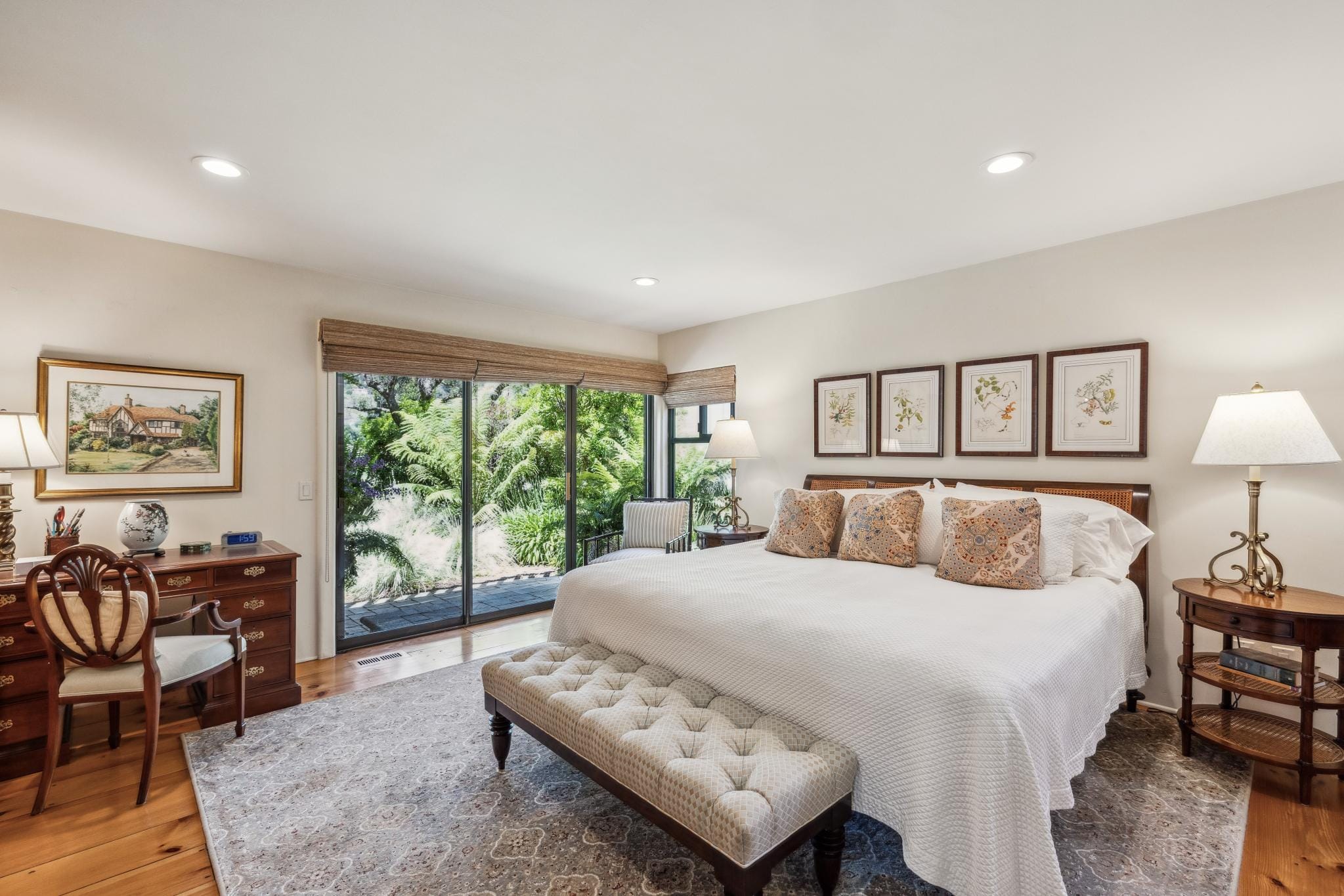 A bedroom with sliding glass doors to garden, wood bed frame, tufted bench, and hardwood floors in Carmel Valley Ranch.
