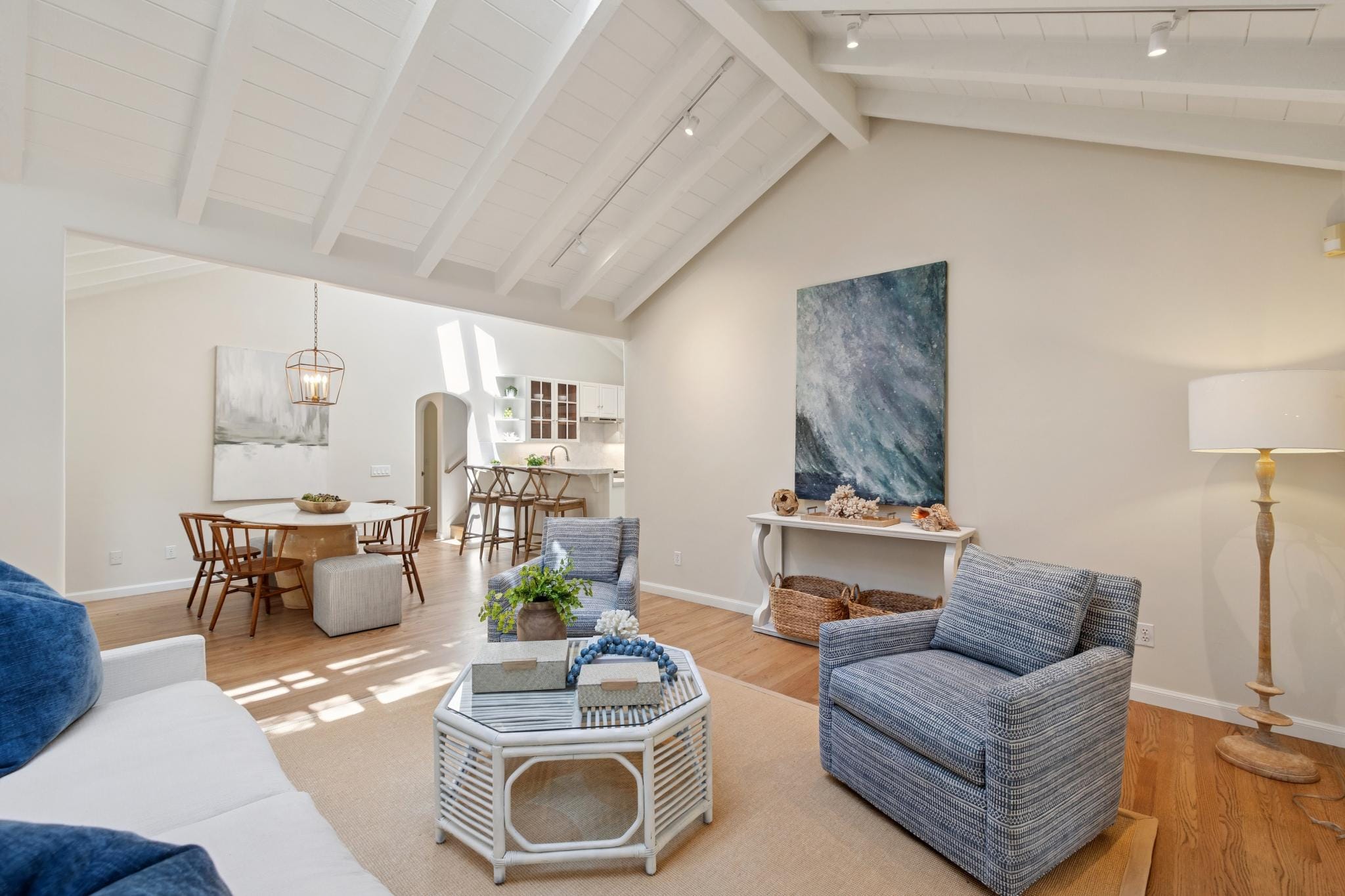 Bright living room with white vaulted beamed ceiling, hardwood floors, blue accent chairs, and open kitchen views in Carmel, CA.