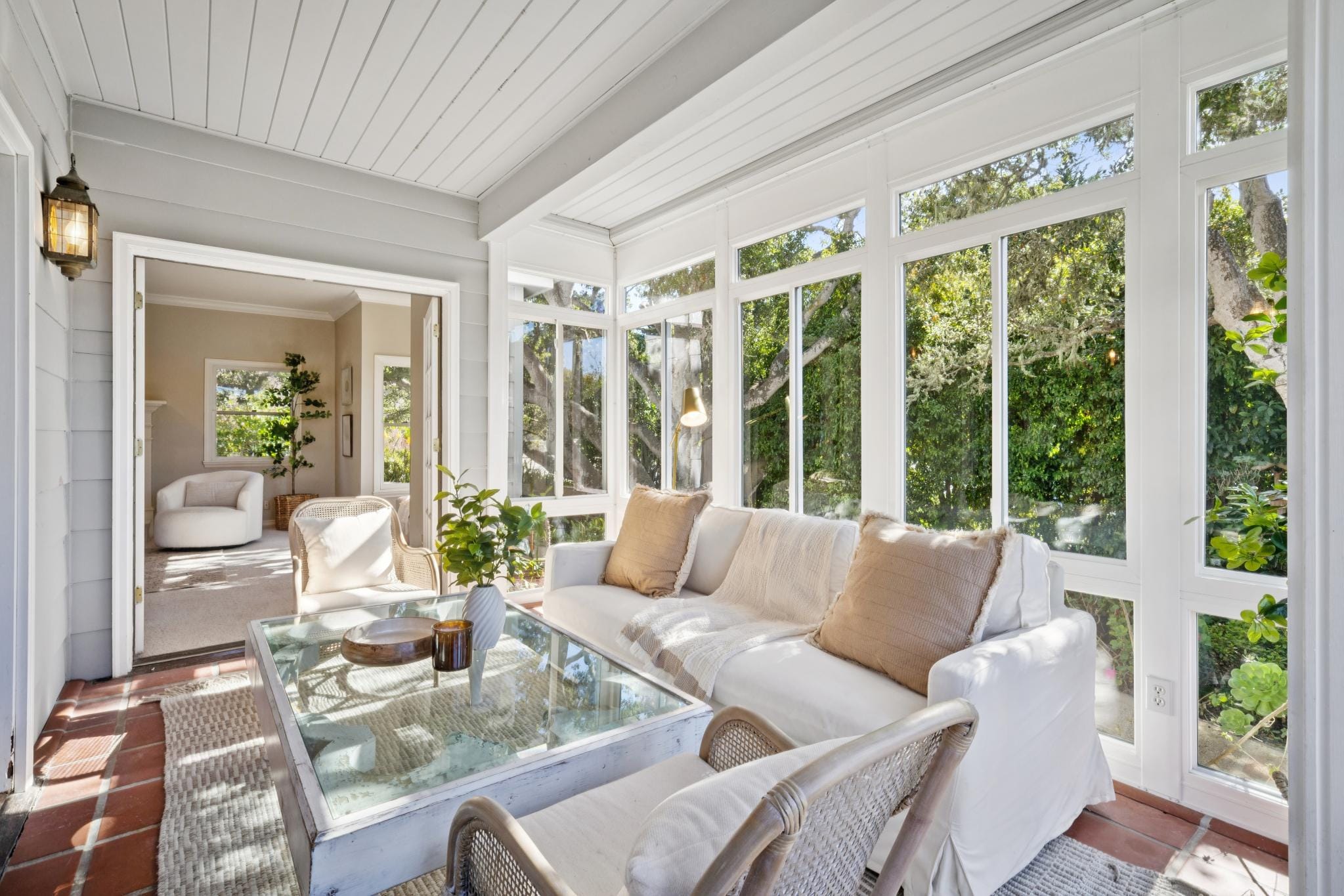 Bright sunroom with floor-to-ceiling windows, white slipcovered sofa, tile floor, and garden views in a Carmel-by-the-Sea home.