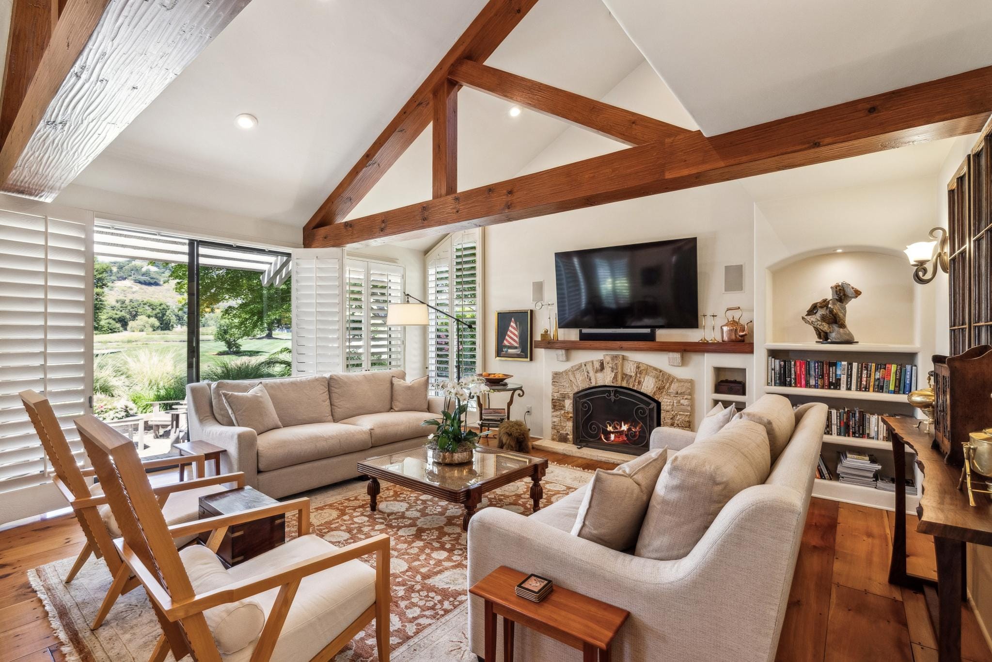 Family room with exposed wood beam ceiling, stone fireplace, golf course views, and built-in shelving in Carmel Valley Ranch.