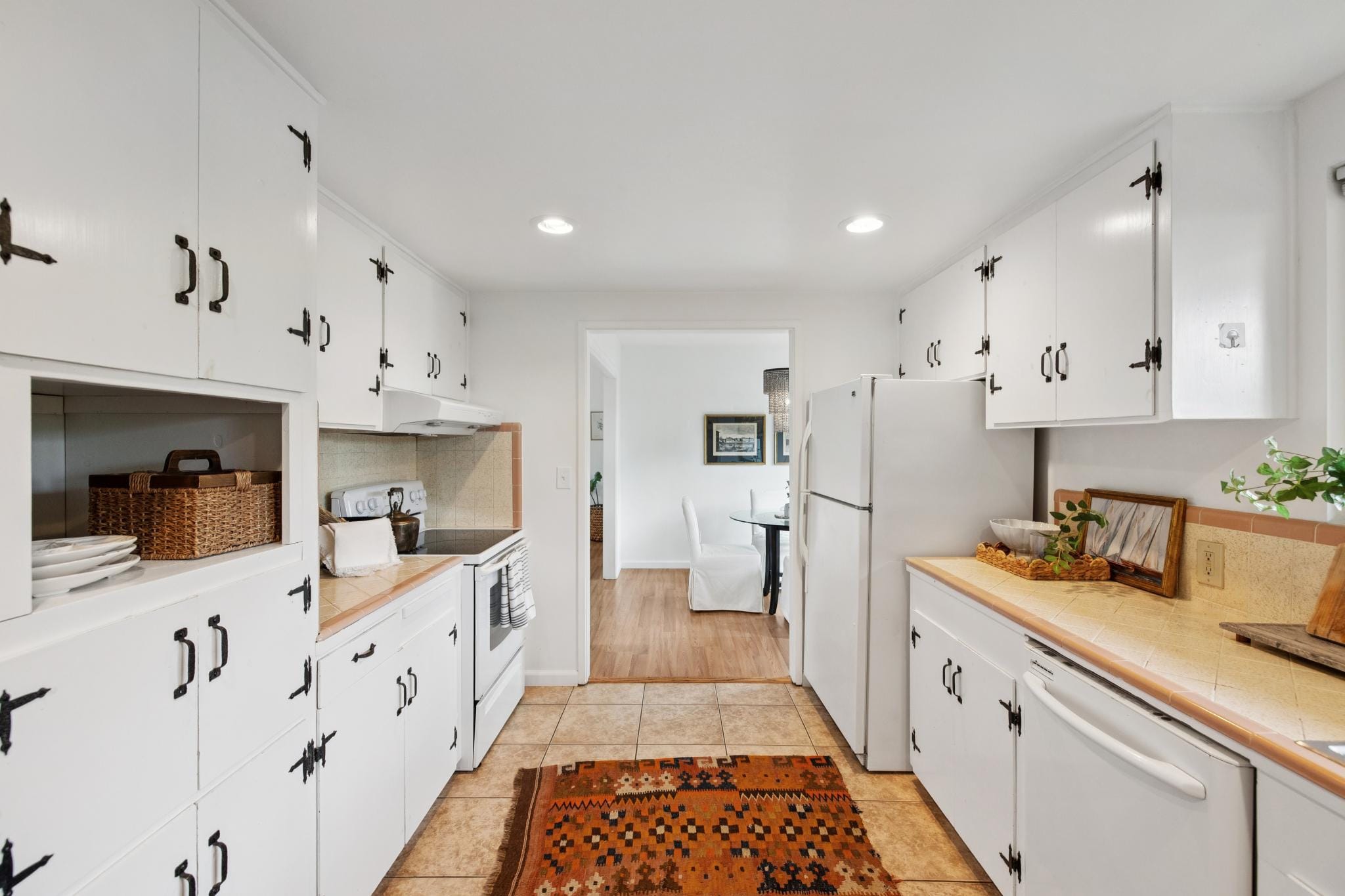 Galley kitchen with white cabinets, black hardware, and kilim runner rug in a Carmel-by-the-Sea cottage.