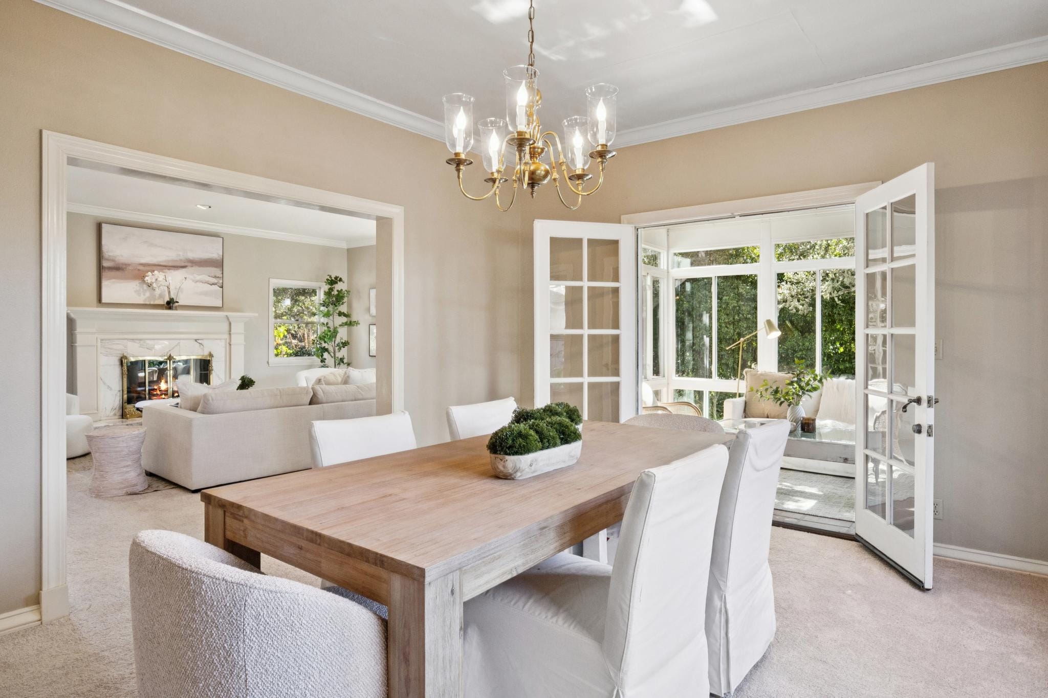 Formal dining room with wood table, chandelier, and French doors to sunroom in a Carmel-by-the-Sea home.