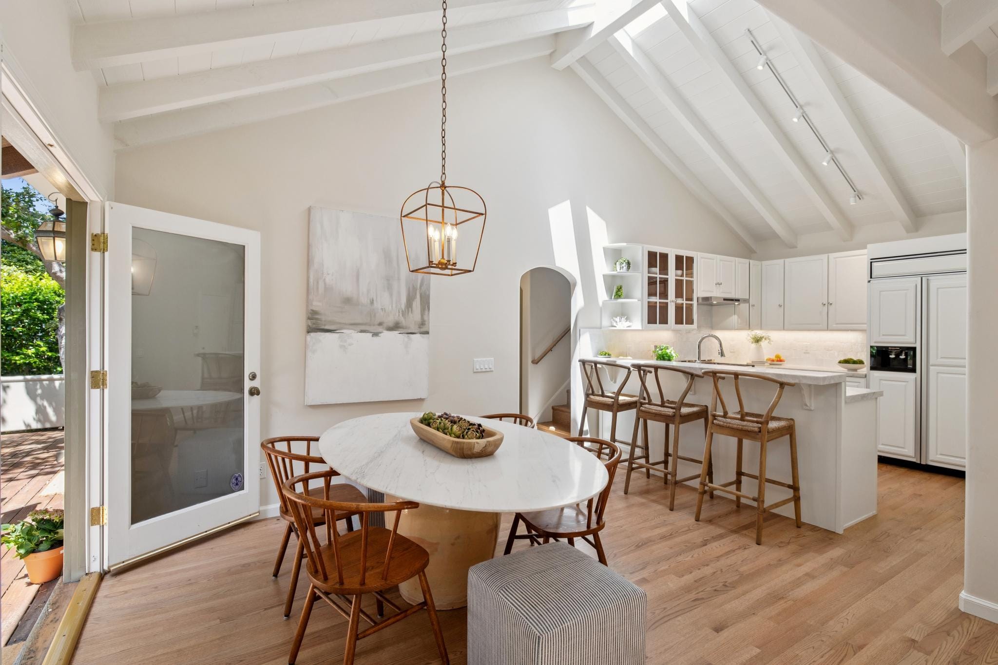 Open-concept dining and kitchen with vaulted beamed ceiling, marble dining table, gold pendant light, and white cabinetry in Carmel, CA.