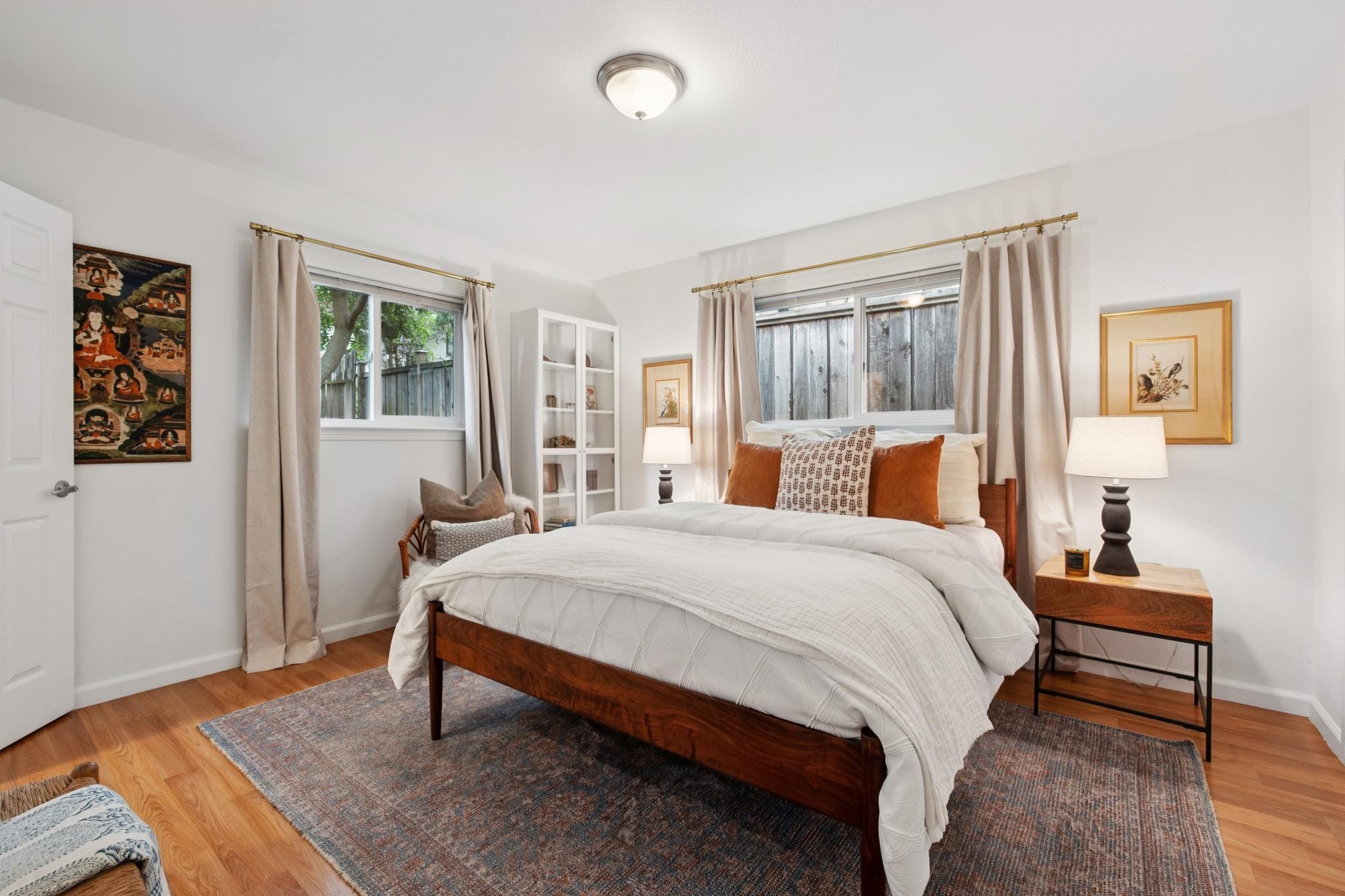 Sunlit bedroom with hardwood floors, wooden bed frame, and linen curtains in a Carmel-by-the-Sea cottage.