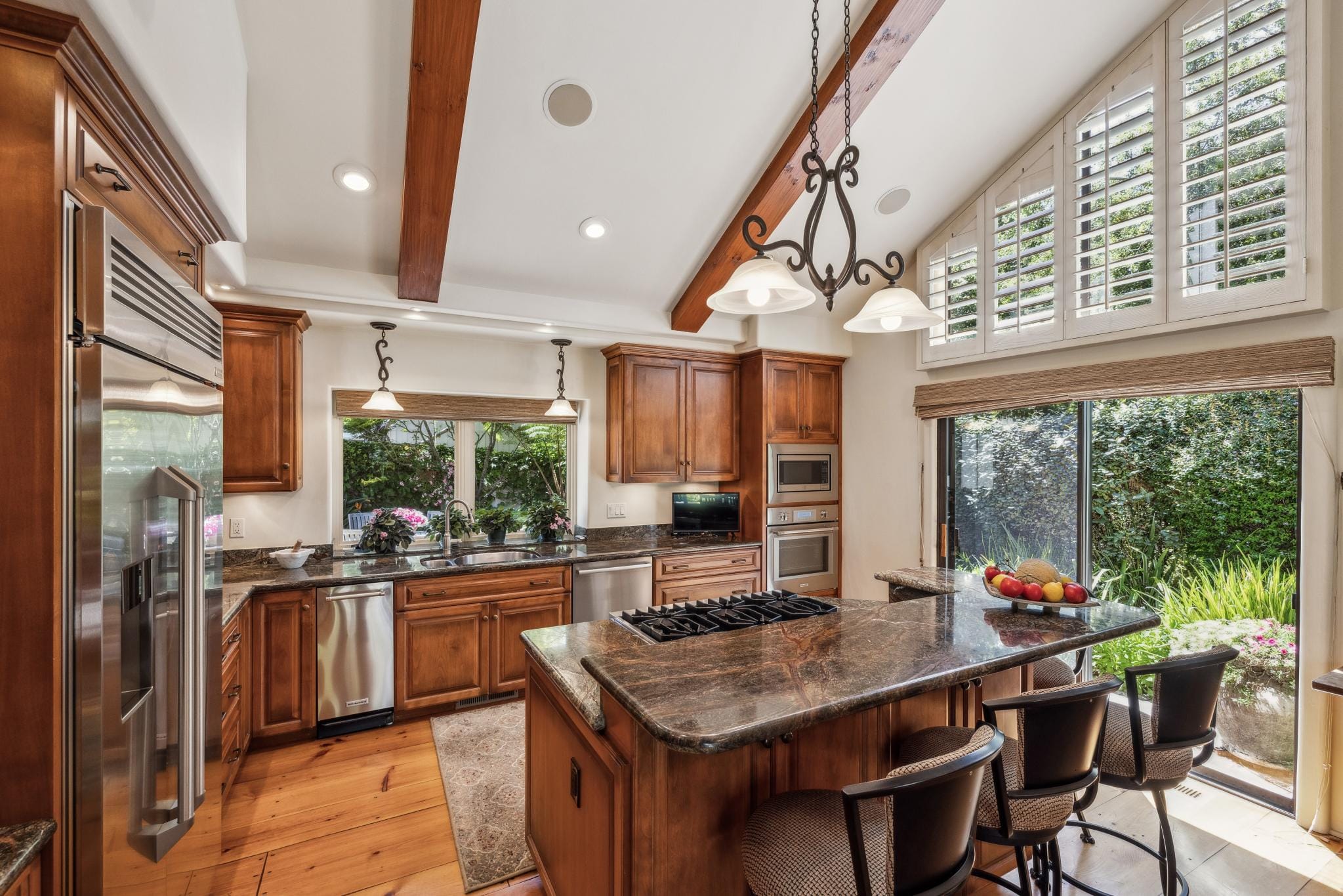 Kitchen with warm wood cabinetry, granite island with gas cooktop, stainless appliances, and wood beam ceiling in Carmel Valley Ranch.