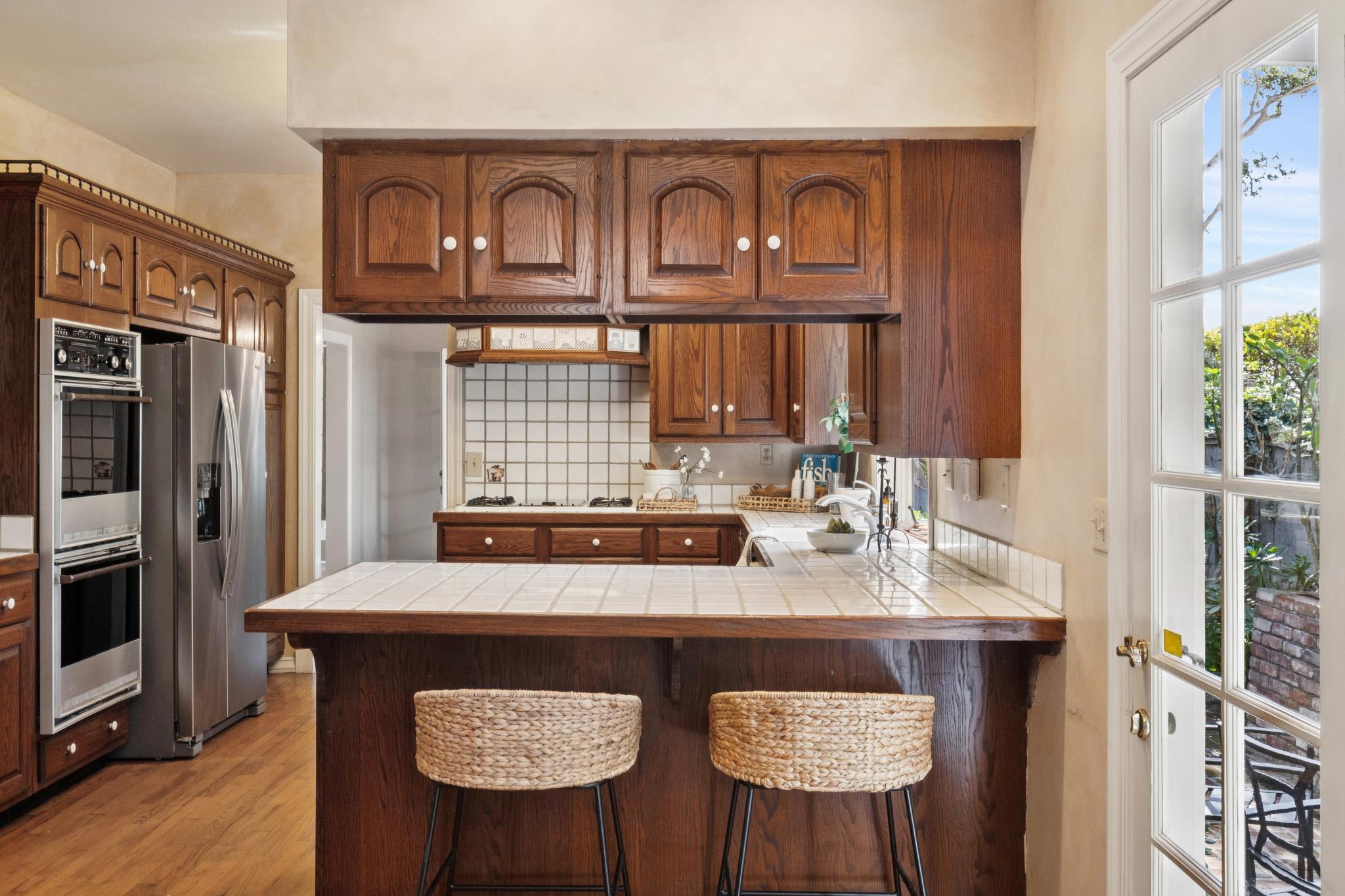 Kitchen with dark wood cabinetry, tile countertops, sit-up bar, and stainless appliances in a Carmel-by-the-Sea home.