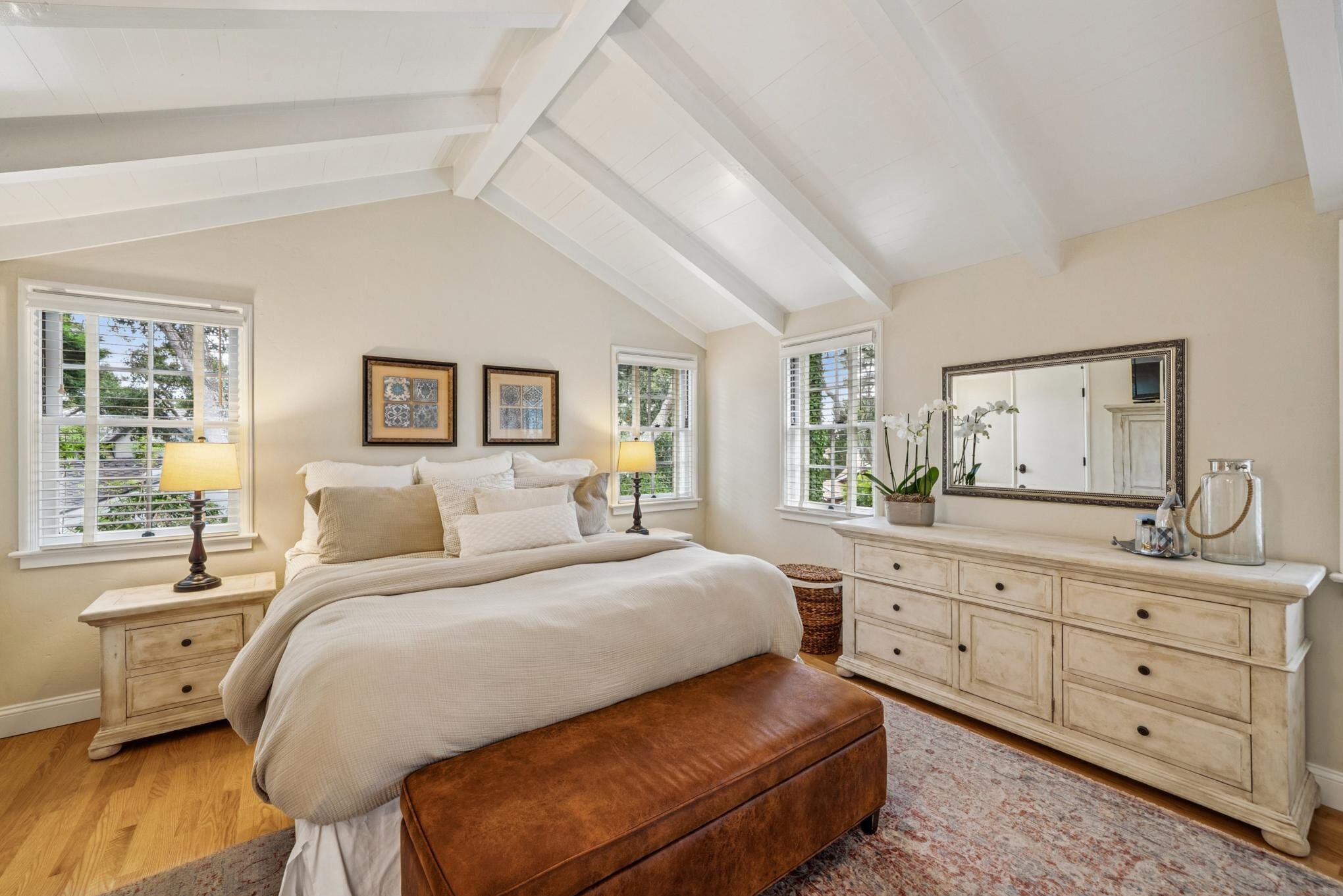 Primary bedroom with vaulted beamed ceiling, hardwood floors, and whitewashed dresser in Carmel, CA.