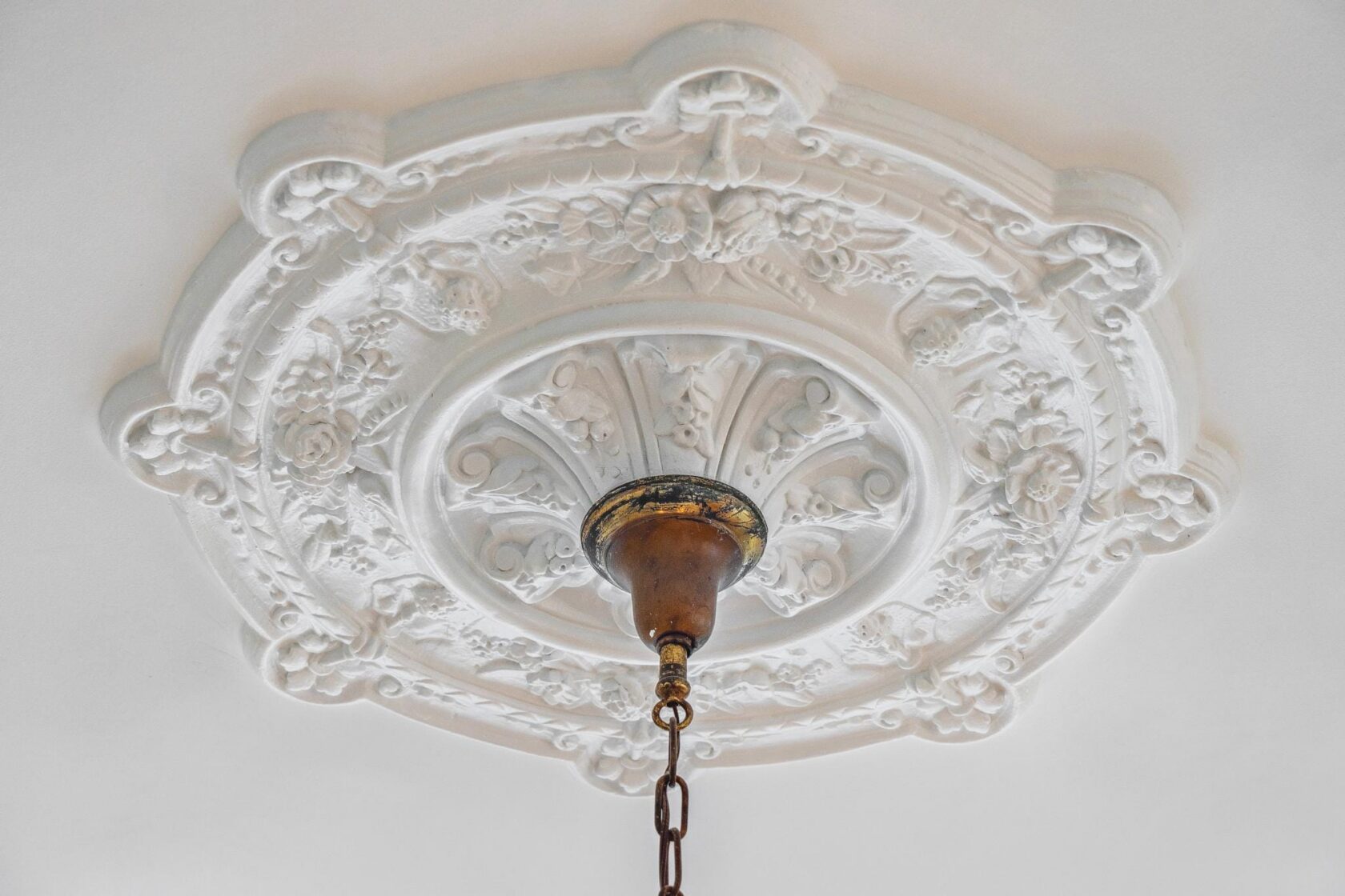 Overhead view of an elaborately detailed original plaster ceiling medallion with floral work, centered by an aged brass canopy and hanging brass chain.