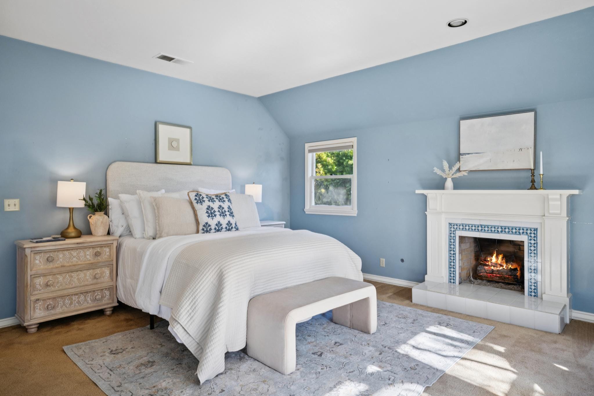 Primary bedroom with blue walls and fireplace with blue tile surround in Carmel-by-the-Sea.