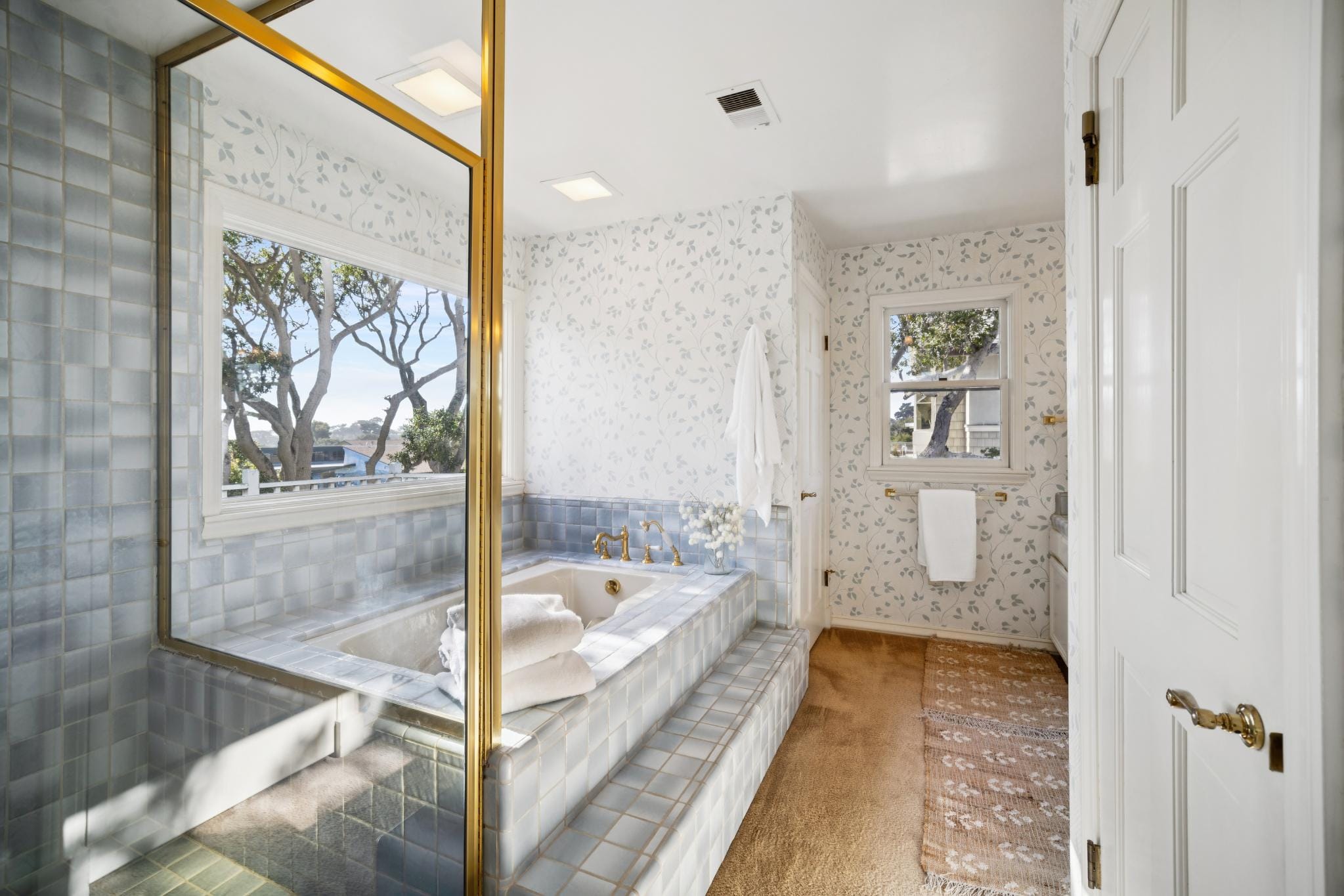 Primary bathroom with soaking tub, blue tile surround, gold fixtures, and floral wallpaper in a Carmel home.