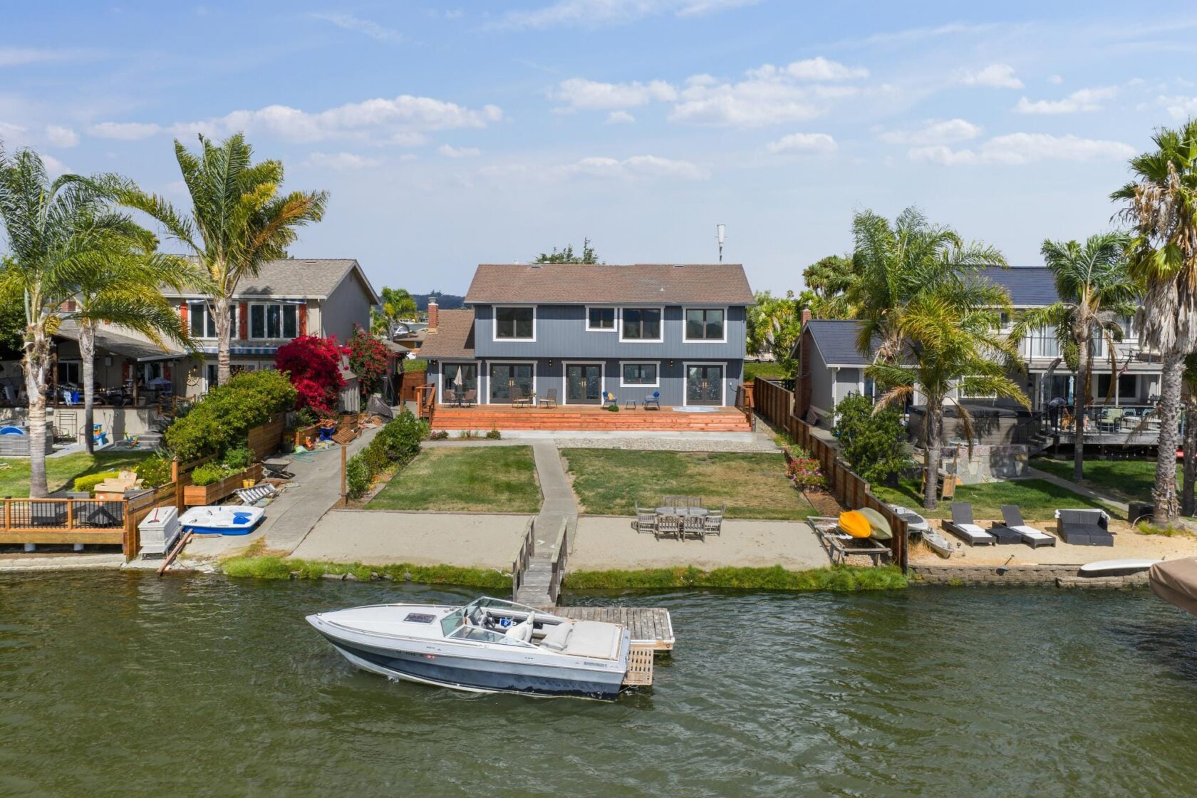 Aerial photograph of 1066 Bel Marin Keys Blvd in Novato, showing a waterfront home with a private pier, landscaped yard, and a boat docked in the Bel Marin Keys waterway, with palm trees and neighboring properties visible.