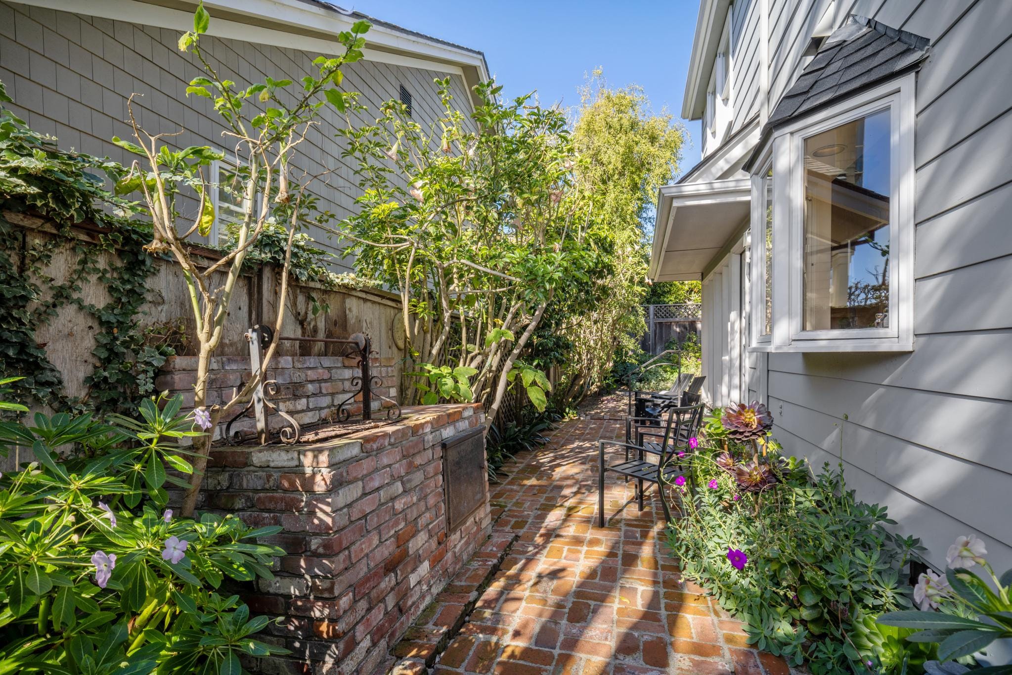 Brick paved side courtyard with brick BBQ, seating, and lush greenery in Carmel-by-the-Sea.
