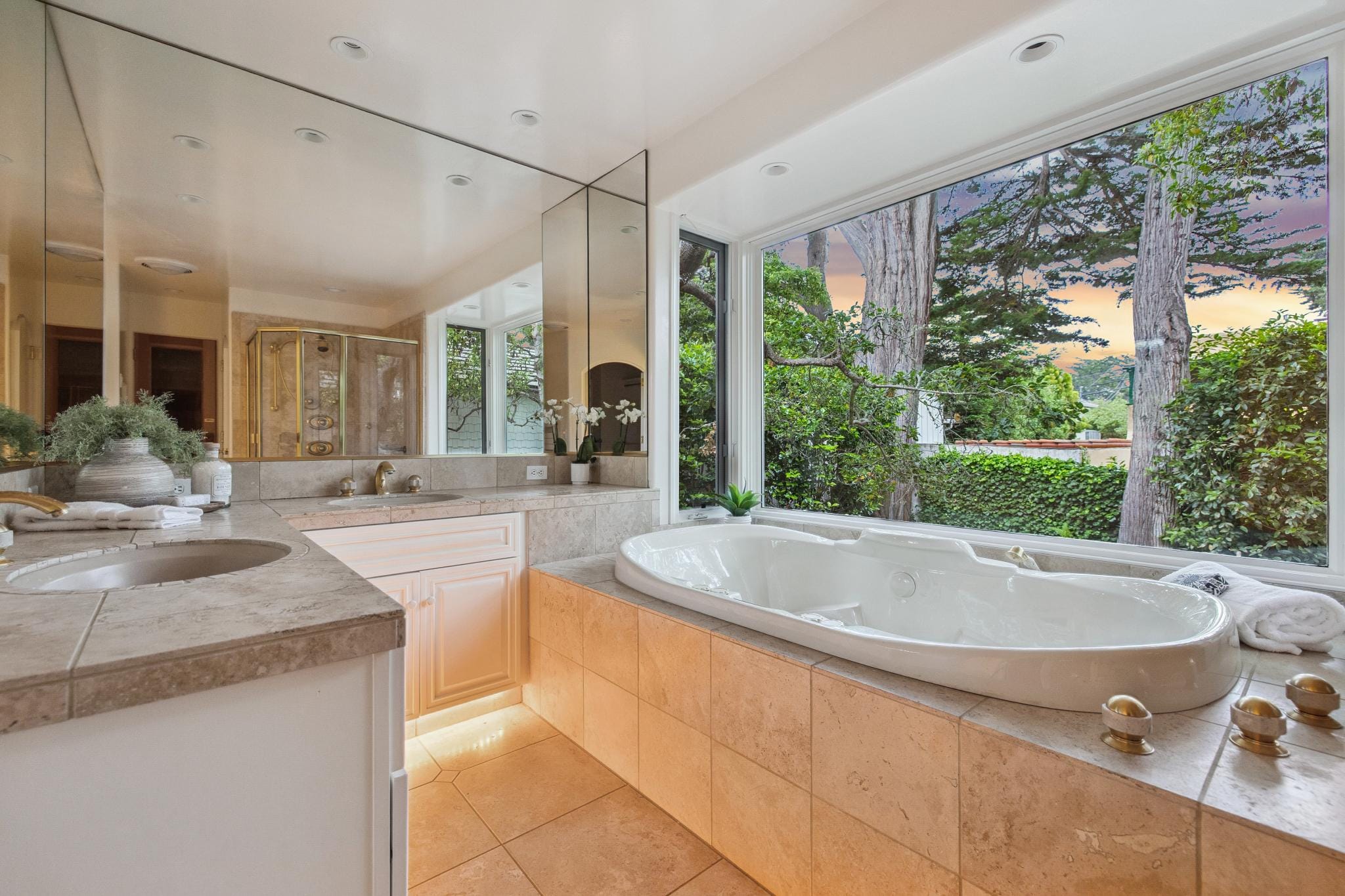 Primary bathroom with Jacuzzi tub, marble tile surround, dual vanity, and tree views in a Carmel, CA cottage.