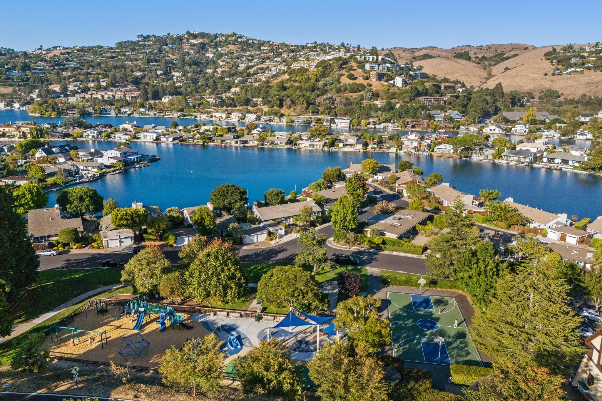 Aerial view of Tiburon lagoon neighborhood with waterfront homes, community playground, and basketball court surrounded by Marin hills
