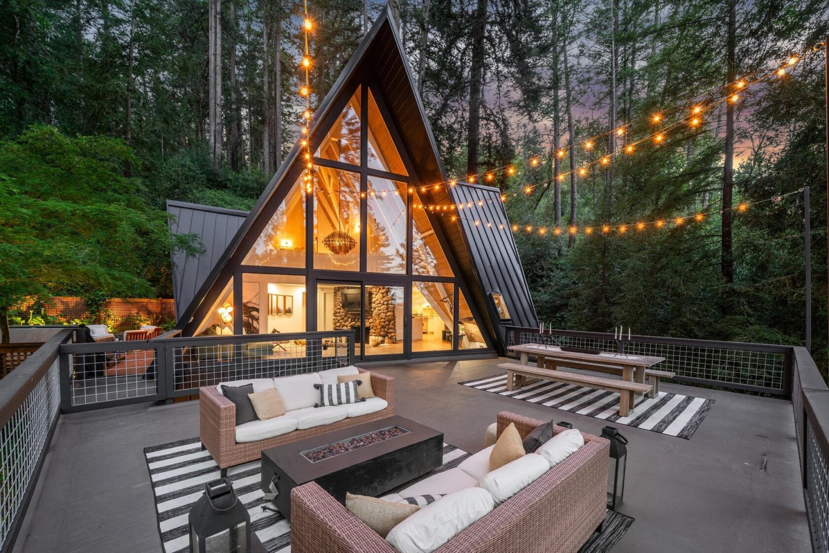 A-frame home at twilight with every interior light and deck string light turned on for a twilight shoot
