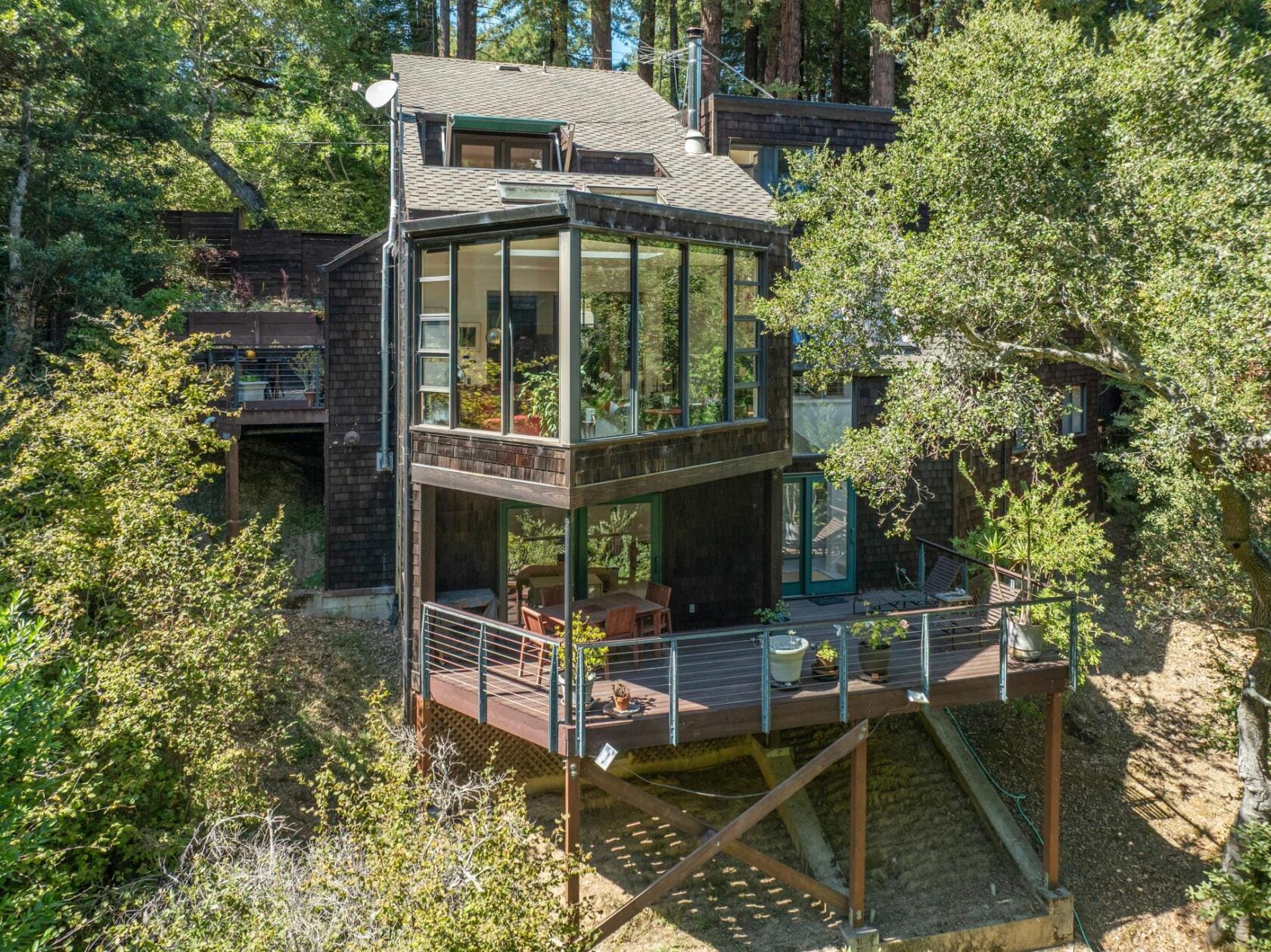 Aerial photograph of 363 Marion Avenue in Mill Valley, showing a multi-level wood-sided home with glass walls and a deck, nestled within a dense redwood forest canopy.