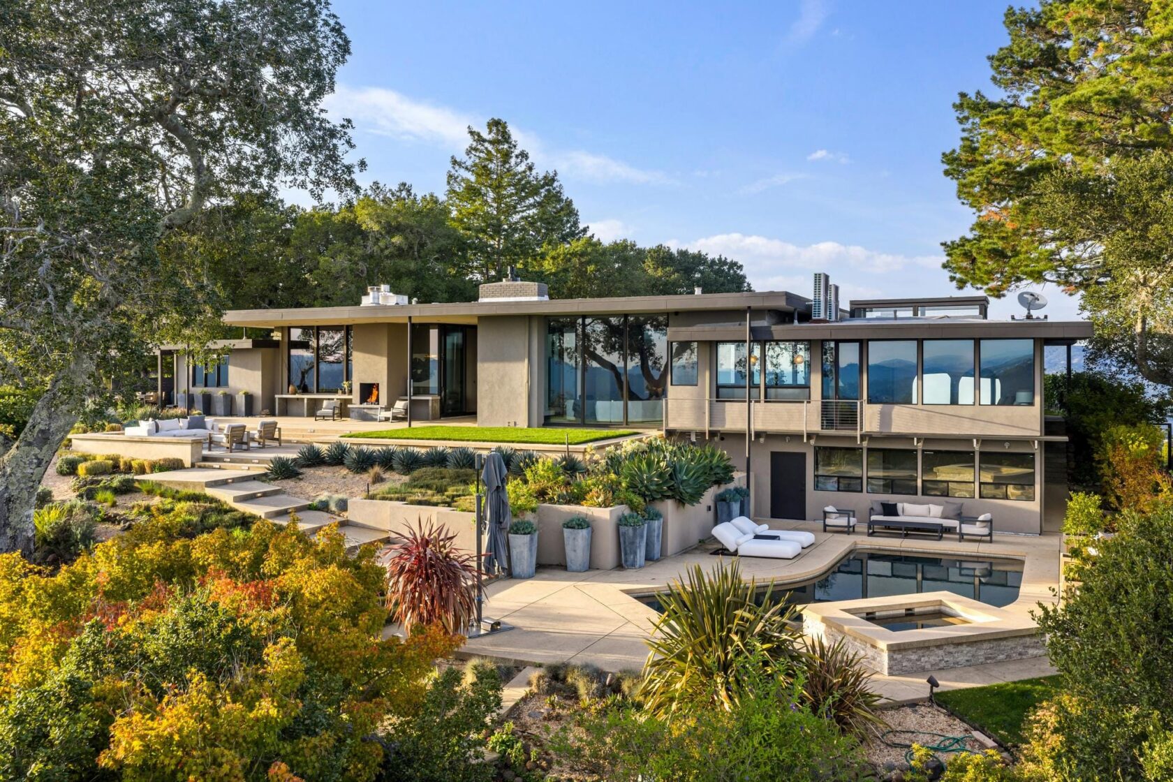 Aerial photograph of 87 Oakmont Avenue in San Rafael, showing a modern hillside home with an outdoor fireplace, pool, spa, lounge seating, and terraced garden areas spanning multiple levels.