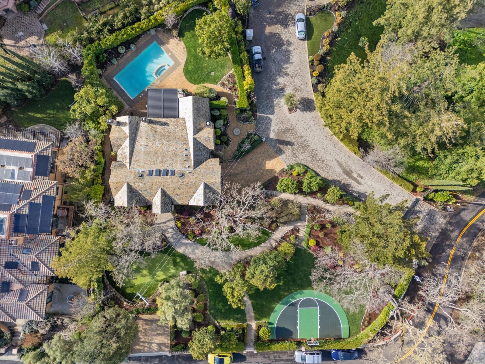  Top-down aerial photograph of 90 Reservoir Road in Los Gatos, showing a large estate with a swimming pool, basketball court, putting green, fountain, and mature landscaping on a wooded lot.