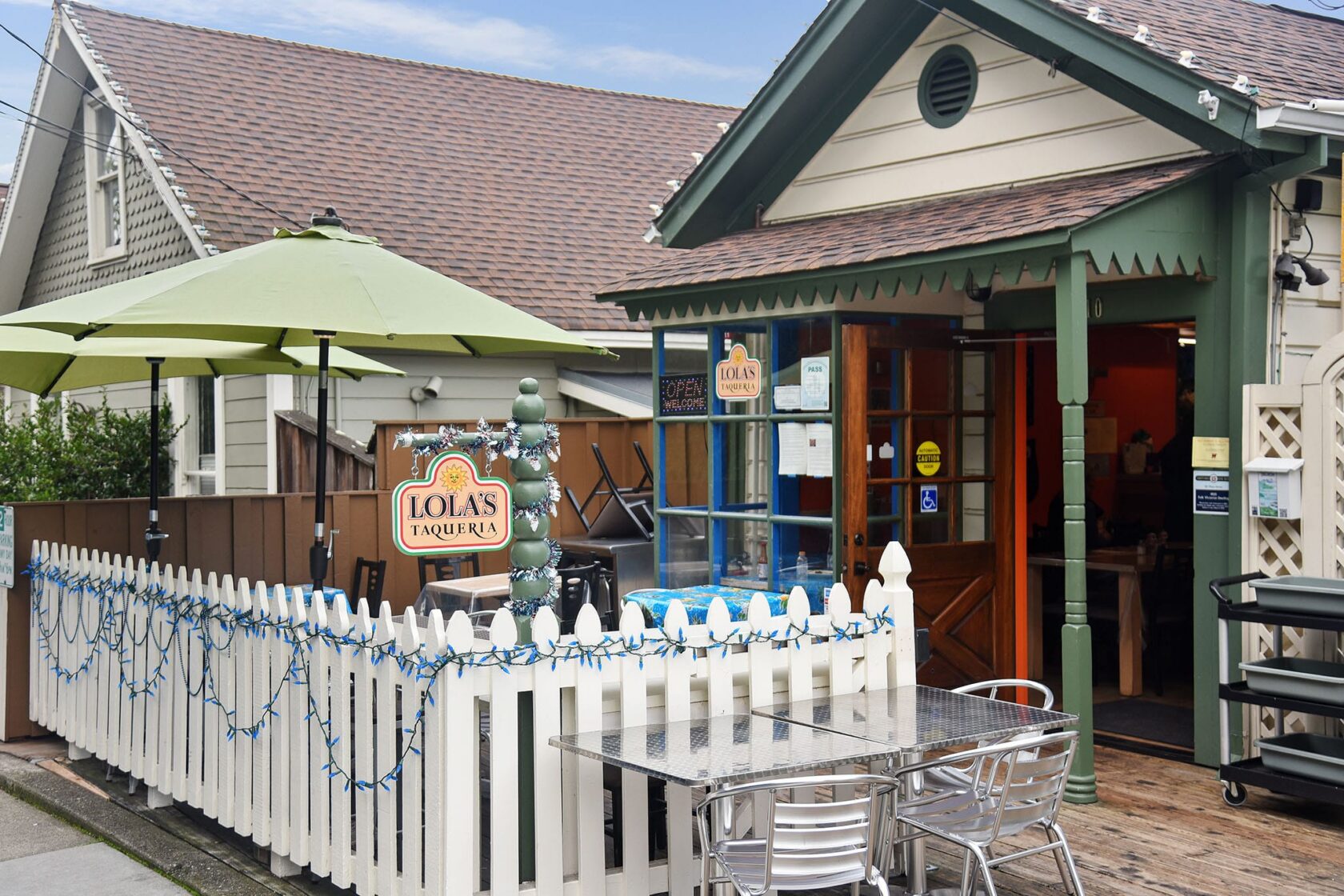 Exterior of Lola's Taqueria in Belvedere CA with white picket fence patio and green umbrella

